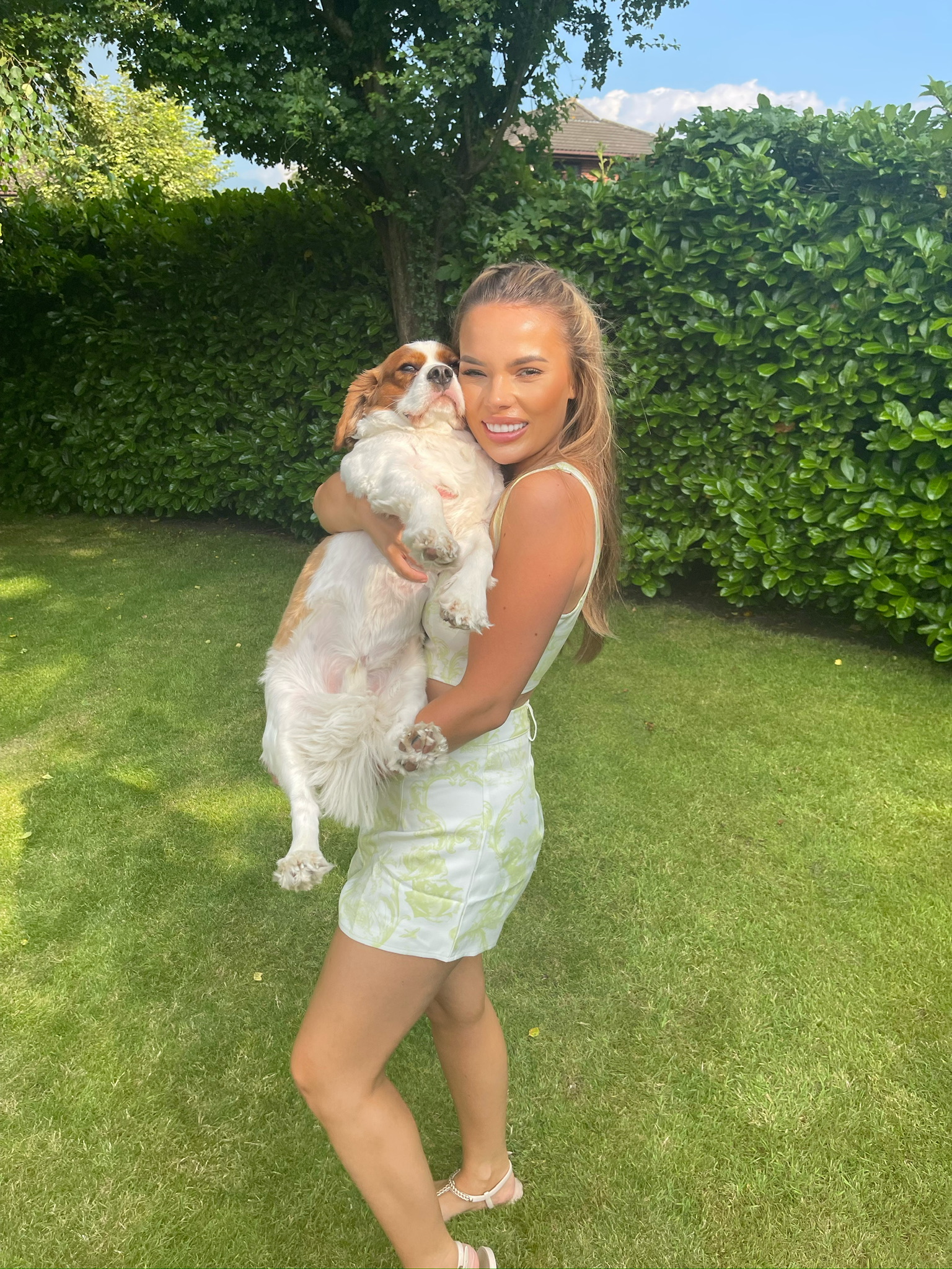 Mariella smiling in a sunny garden holding Marley, her Cavalier King Charles Spaniel